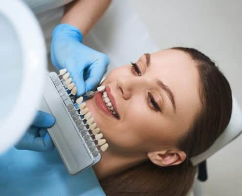 cheerful-young-lady-is-lying-dental-chair-choosing-veeners-colour-with-doctor-help